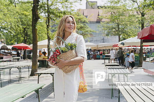 Happy woman holding bags of groceries in farmer's market
