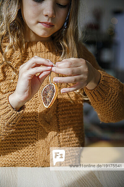 Girl tying thread on dried lemon at table