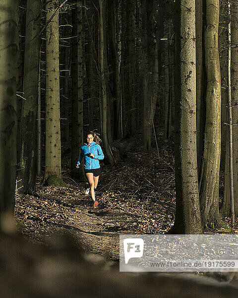 Young sportswoman running in forest at dusk