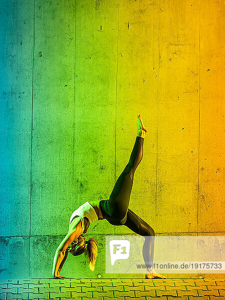 Woman doing yoga near neon colored wall