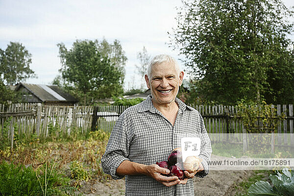 Smiling man holding onions in garden