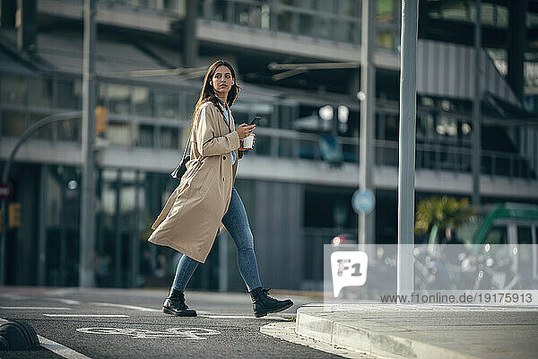 Young woman walking with smart phone and coffee cup at street