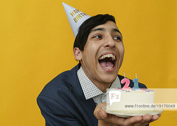 Cheerful man holding 21st birthday cake in studio