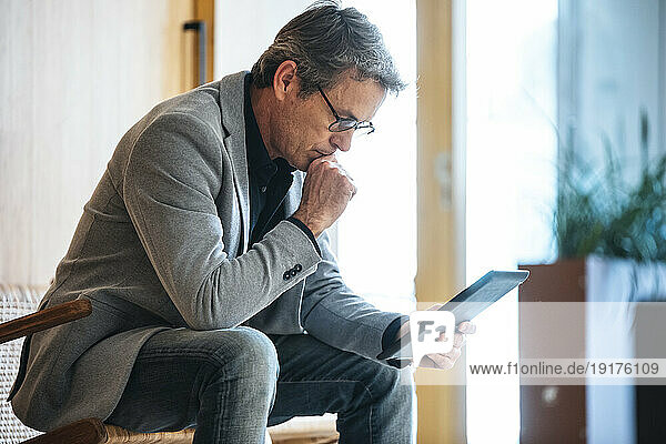 Businessman with hand on chin using tablet PC in office