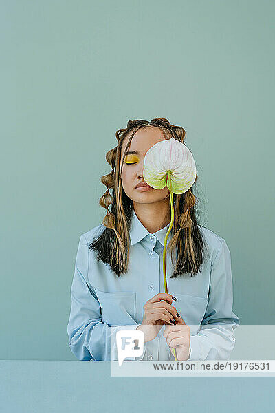 Young woman with eyes closed holding flower against blue background