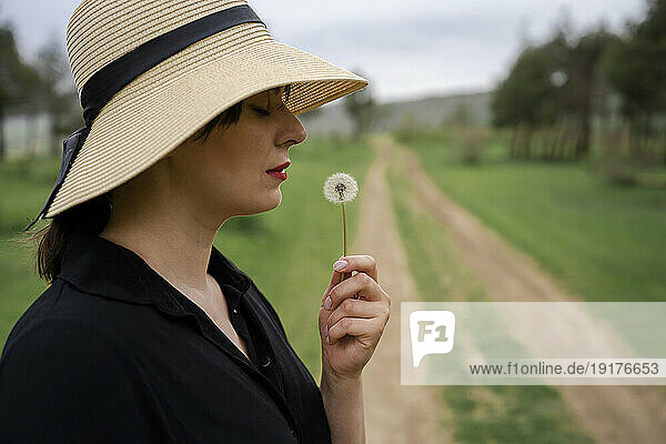 Young woman with straw hat smelling dry dandelion