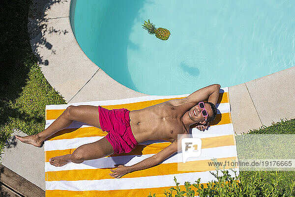 Happy man relaxing on striped towel by poolside