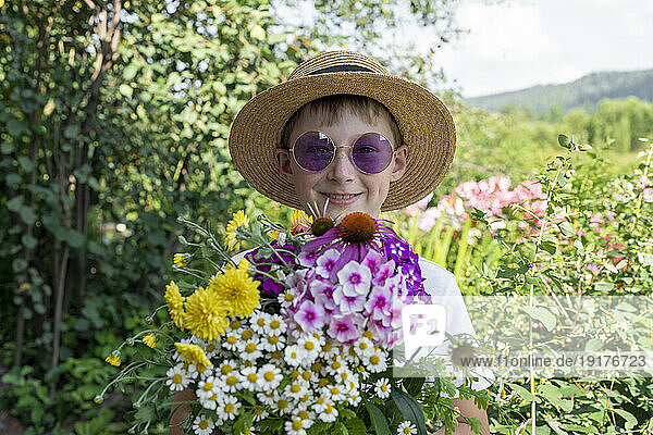 Happy boy wearing hat holding various flowers in garden