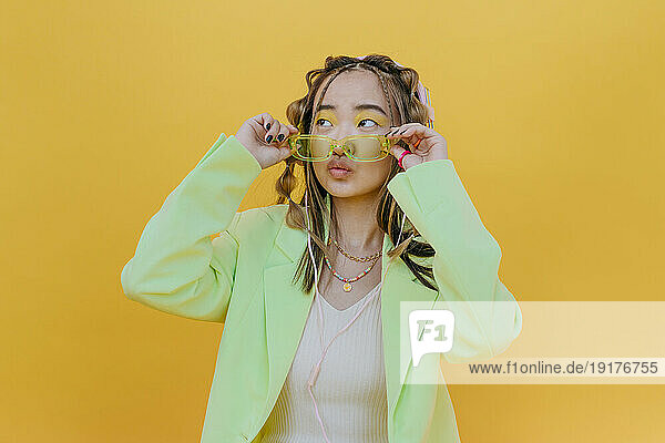 Young woman wearing sunglasses and puckering against yellow background in studio