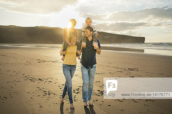 Happy mother and father carrying children on shoulders at sunset