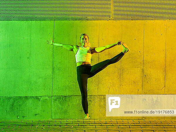 Happy woman doing yoga in front of neon colored wall