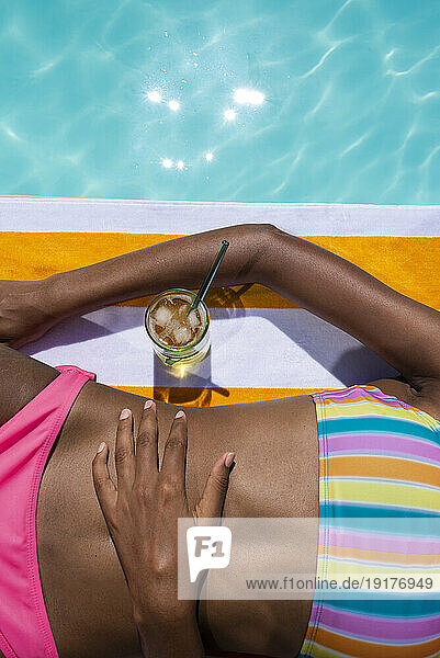 Woman with drink lying near pool
