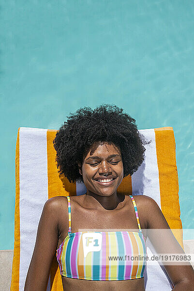 Smiling woman lying on stripped towel with eyes closed in pool