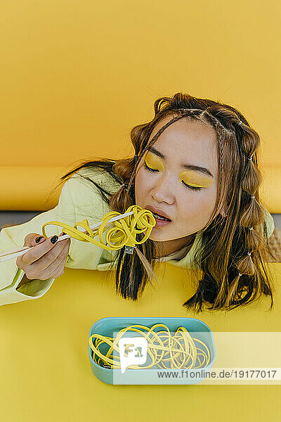 Young woman eating wired noodles at table in studio
