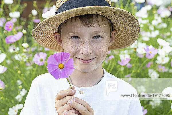 Smiling boy wearing hat holding flower in garden