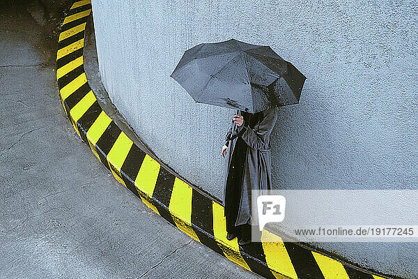 Woman holding umbrella standing near wall