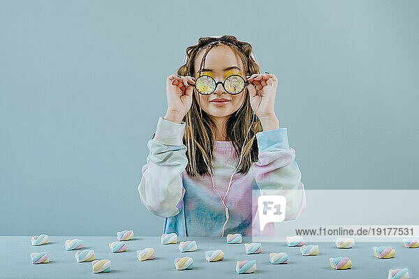 Woman wearing kaleidoscope glasses at table with marshmallows in studio