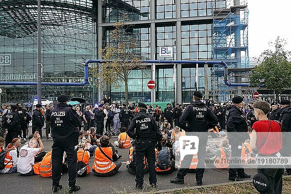 Straßenblockade der letzten Generation am Berliner Hauptbahnhof  umringt von der Polizei. Im Hintergrund die Glasfassade des Hauptbahnhofs