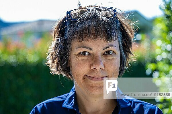 Headshot einer glücklich lächelnden Frau mit Brille  die an einem sonnigen Tag in der Schweiz in die Kamera schaut