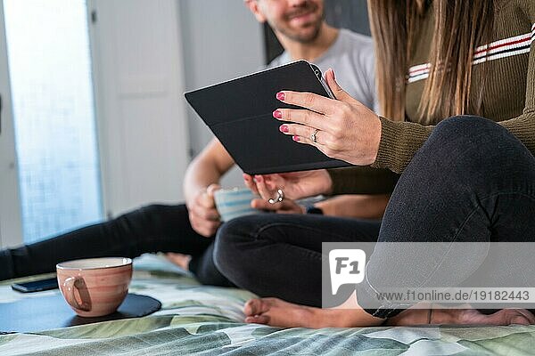 Nahaufnahme der Hände und Beine eines nicht erkennbaren Paares  das entspannt auf dem Bett ein Tablet benutzt