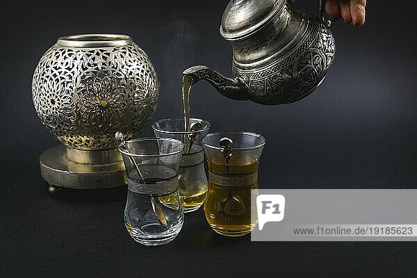 Servieren von maurischem Tee aus einer Metalltasse zu drei Gläsern  einer Tasse und türkischen Schüsseln
