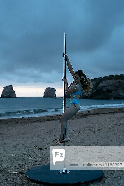 Junges kaukasisches Mädchen macht Pole Dance bei Sonnenaufgang an einem schönen Strand. Pole Dance Akrobatik auf dem Sand von Hendaya Strand  Frankreich. Blaue Zeit als erstes am Morgen