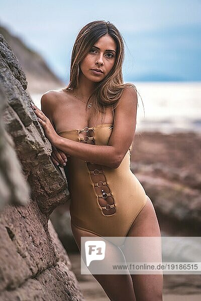Porträt einer brünetten Frau mit Badeanzug auf den Felsen eines Strandes im Sommer  die in die Kamera schaut