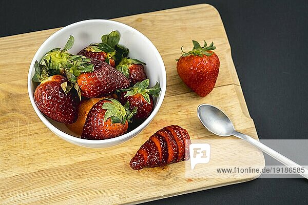 Luftaufnahme einer auf einem Holz geschnittenen Erdbeere und einer weißen Schale mit weiteren Erdbeeren  Rezept für selbstgemachte Erdbeeren