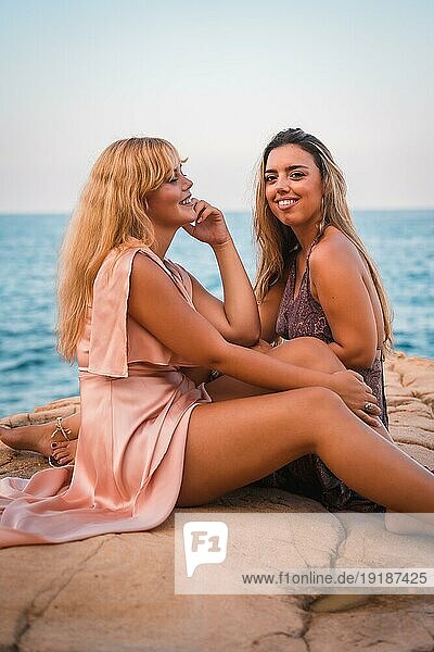 Ein paar kaukasische Mädchen  die Spaß haben  sitzen in sehr schönen Kleidern und genießen den Sommer am Meer  vertikales Foto