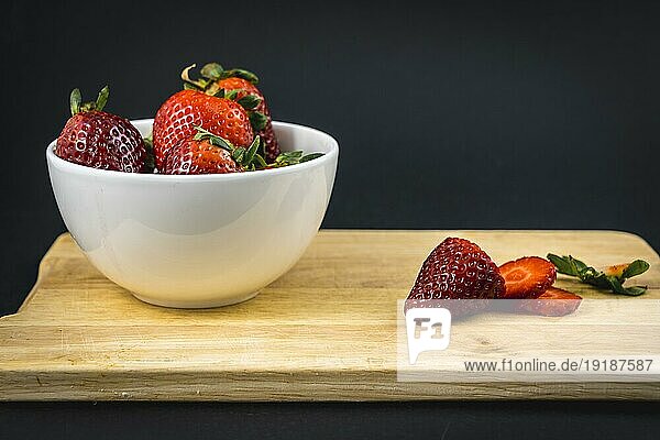 Eine Erdbeere auf einem Holz geschnitten und eine weiße Schale mit mehr Erdbeeren  hausgemachte Erdbeere Rezept