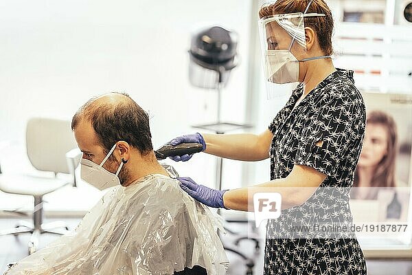 Friseur mit Sicherheitsvorkehrungen für das Covid19 neue Normalität  soziale Distanz  Haare schneiden mit einer Maske und einem Schutzschirm aus Kunststoff