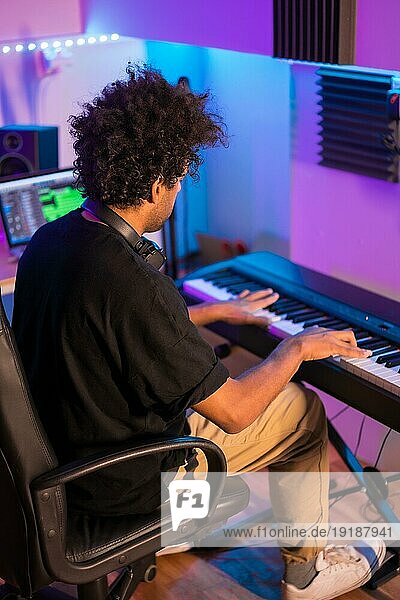 Vertikale Rückansicht eines Klavier spielenden Musikers  der in einem Produktionsstudio sitzt