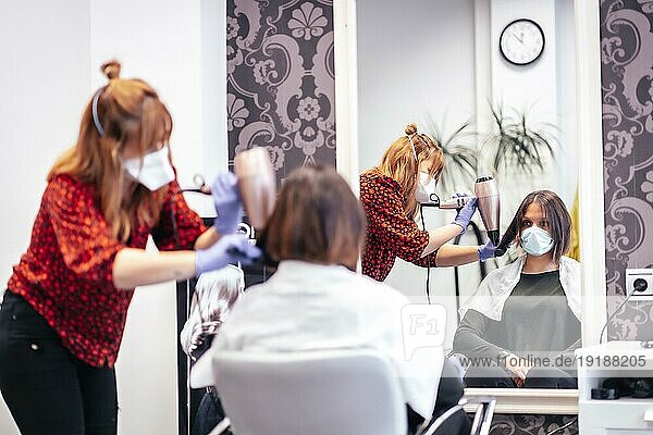 Friseur mit Maske und Handschuhen glättet das Haar eines Kunden. Wiedereröffnung mit Sicherheitsmaßnahmen für Friseure im Rahmen der Covid 19 Pandemie