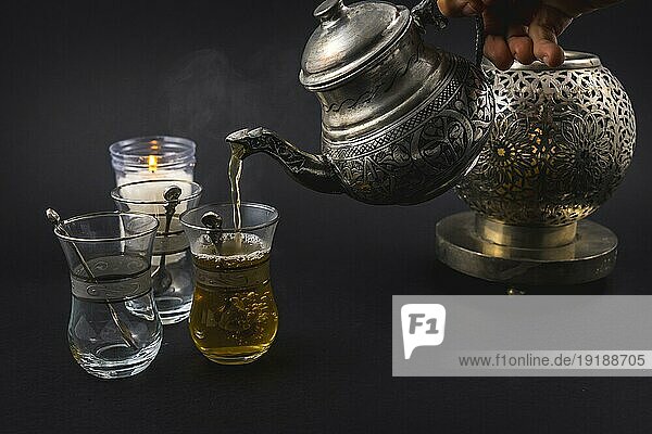 Servieren von maurischem Tee aus einer Metalltasse zu drei Gläsern  einer Tasse und türkischen Schüsseln