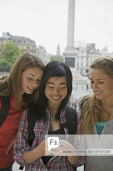 Three smiling teenaged girls using a cell phone in London Trafalgar Square