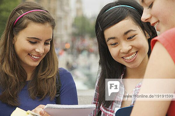 Three smiling teenaged girls reading  writing and holding note pads