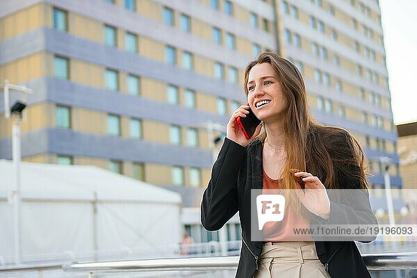 Junge und lässige Geschäftsfrau lächelt  während sie mit dem Handy im Freien spricht