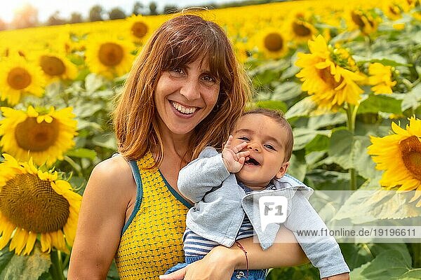 Porträt einer kaukasischen Mutter und ihres lachenden Babys in einer Sonnenblumenlandschaft  Sommer Lifestyle