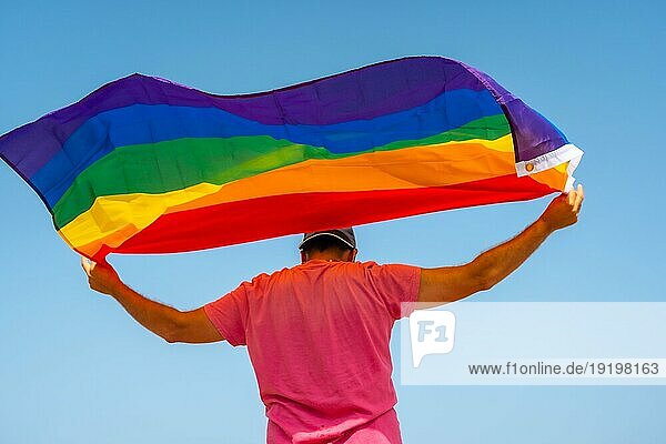Eine schwule Person mit der LGBT Flagge auf dem Rücken  die sich mit dem Wind bewegt  mit dem Himmel im Hintergrund  Symbol der Homosexualität  Regenbogenflagge