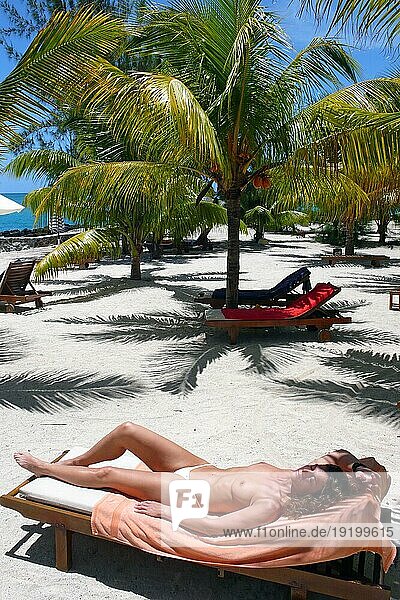 Frau sonnt sich ohne Oberteil oben ohne auf Sonnenliege Strandliege unter Kokospalmen (Cocos nucifera) an Palmenstrand  Karibik
