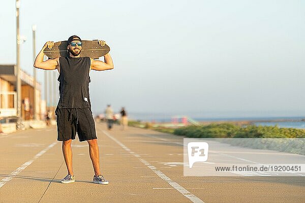 Ein Mann steht auf einem Radweg und trägt ein Skateboard auf den Schultern. Mittlere Einstellung