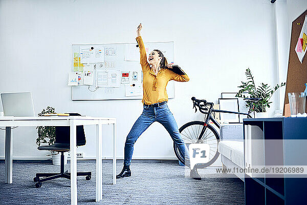 Happy young businesswoman cheering in office