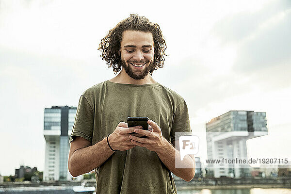 Germany  Cologne  smiling young man looking at cell phone