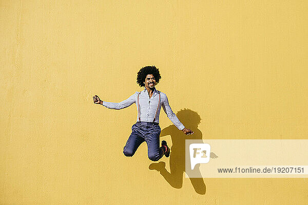 Smiling man jumping in the air in front of yellow wall