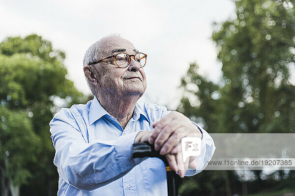 Portrait of senior man in a park leaning on his walking stick