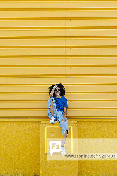 Pretty woman sitting on platform in front of yellow wall  smiling