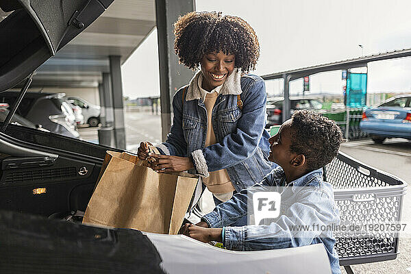 Happy mother and son keeping shopping bags in car trunk