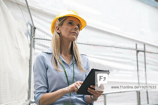 Contemplative engineer looking up holding tablet PC
