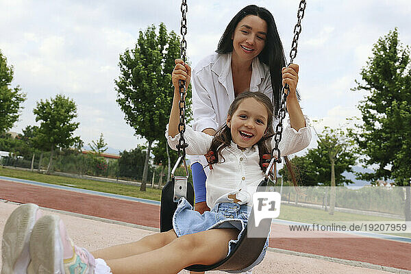 Happy mother with daughter swinging on swing