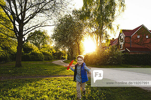 Happy boy running with toy airplane at sunset
